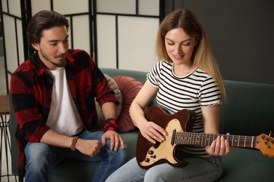 Photo of Tutor teaching woman to play guitar on sofa at home