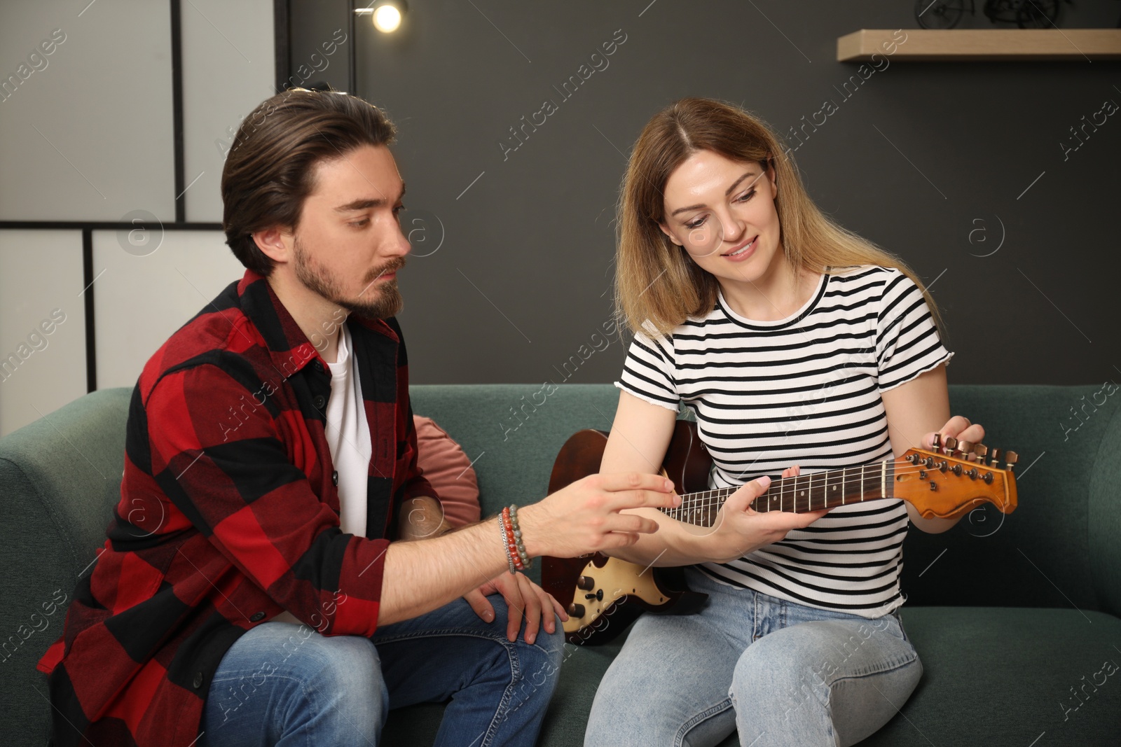 Tutor teaching woman to play guitar on sofa at home Photo of Tutor teaching woman to play guitar on sofa at home