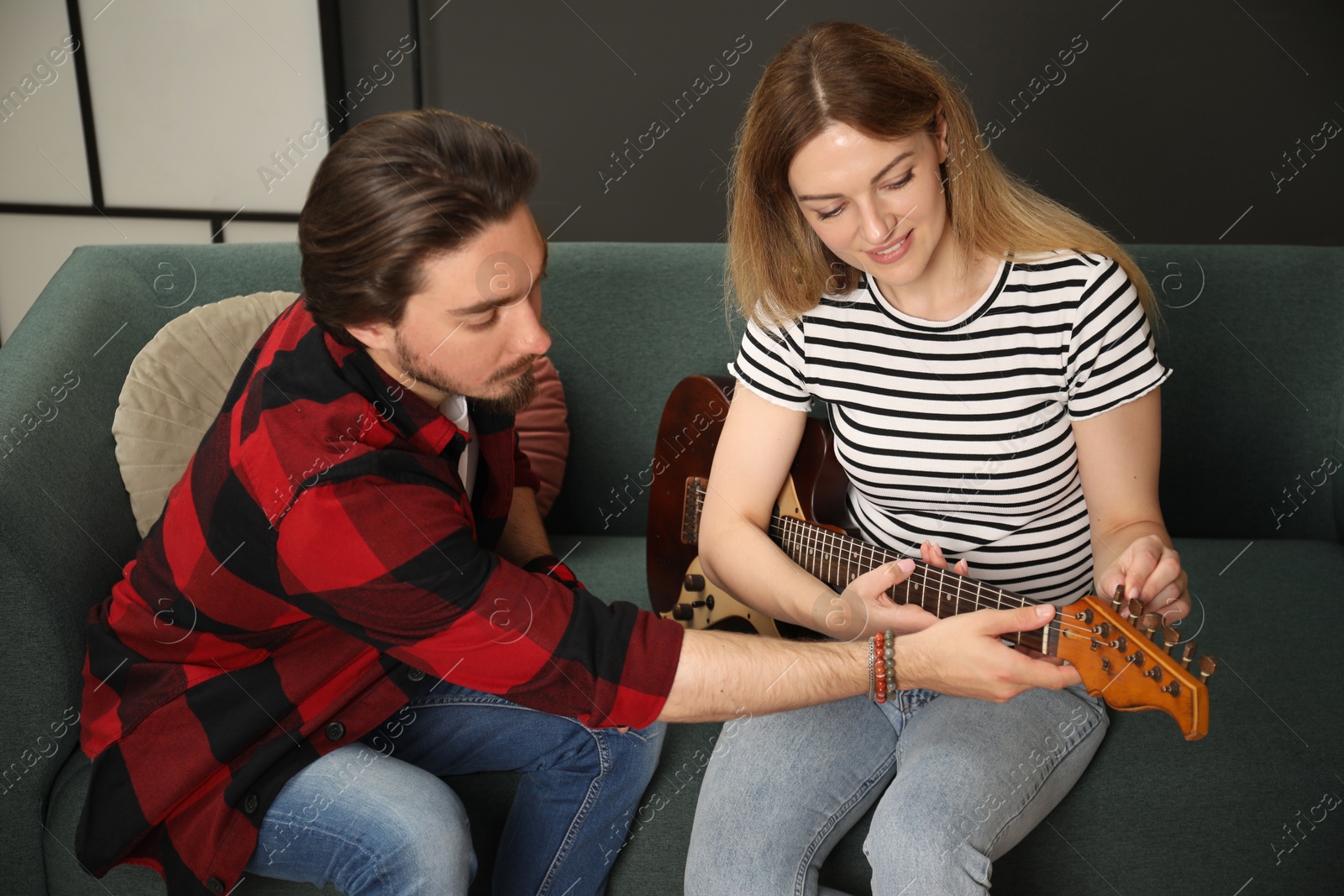 Photo of Tutor teaching woman to play guitar on sofa at home