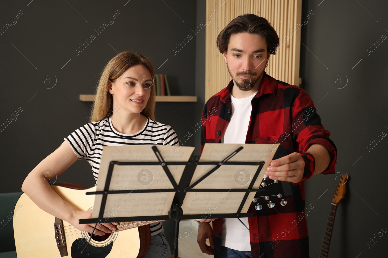 Photo of Tutor teaching woman to play guitar indoors
