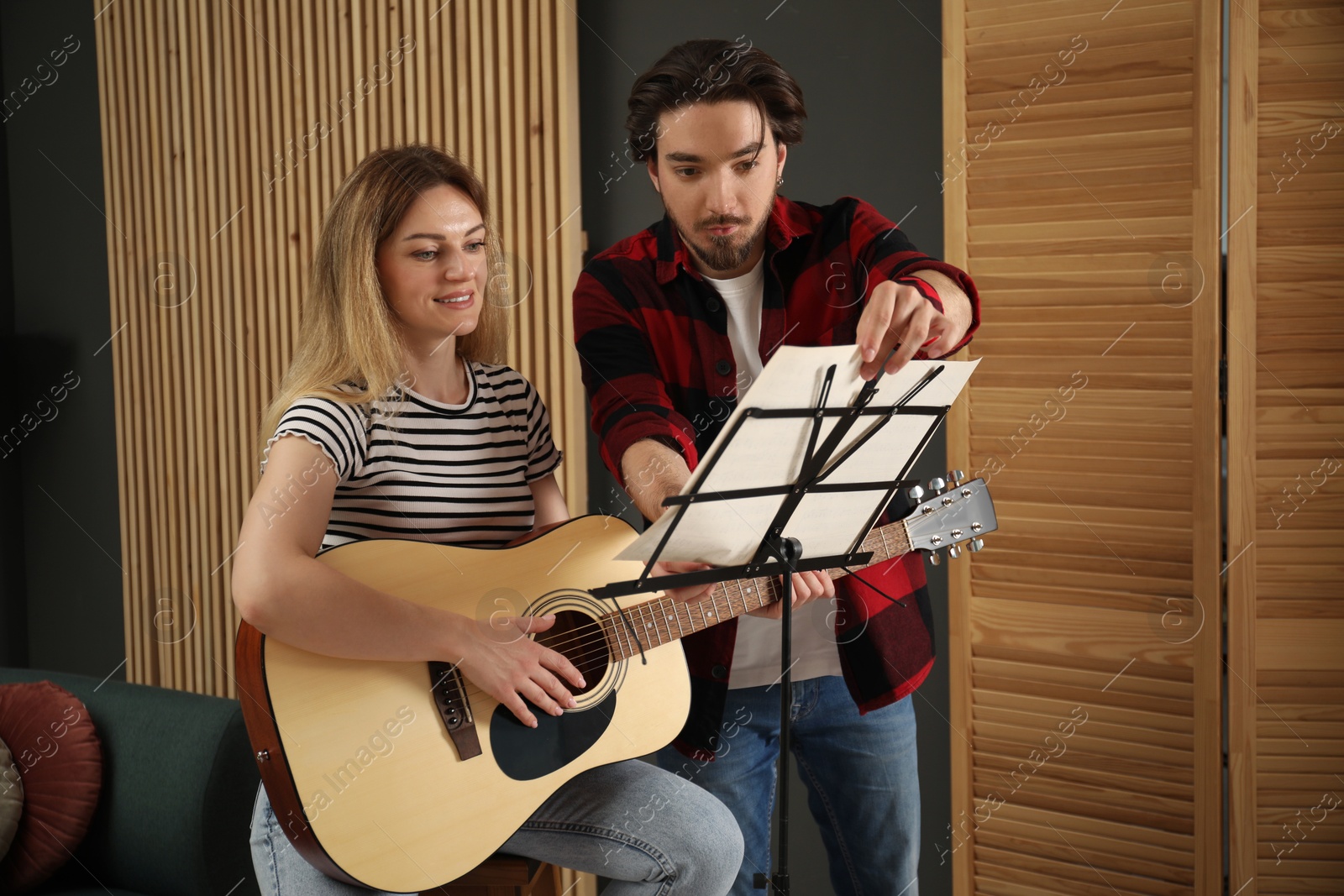 Photo of Tutor teaching woman to play guitar indoors