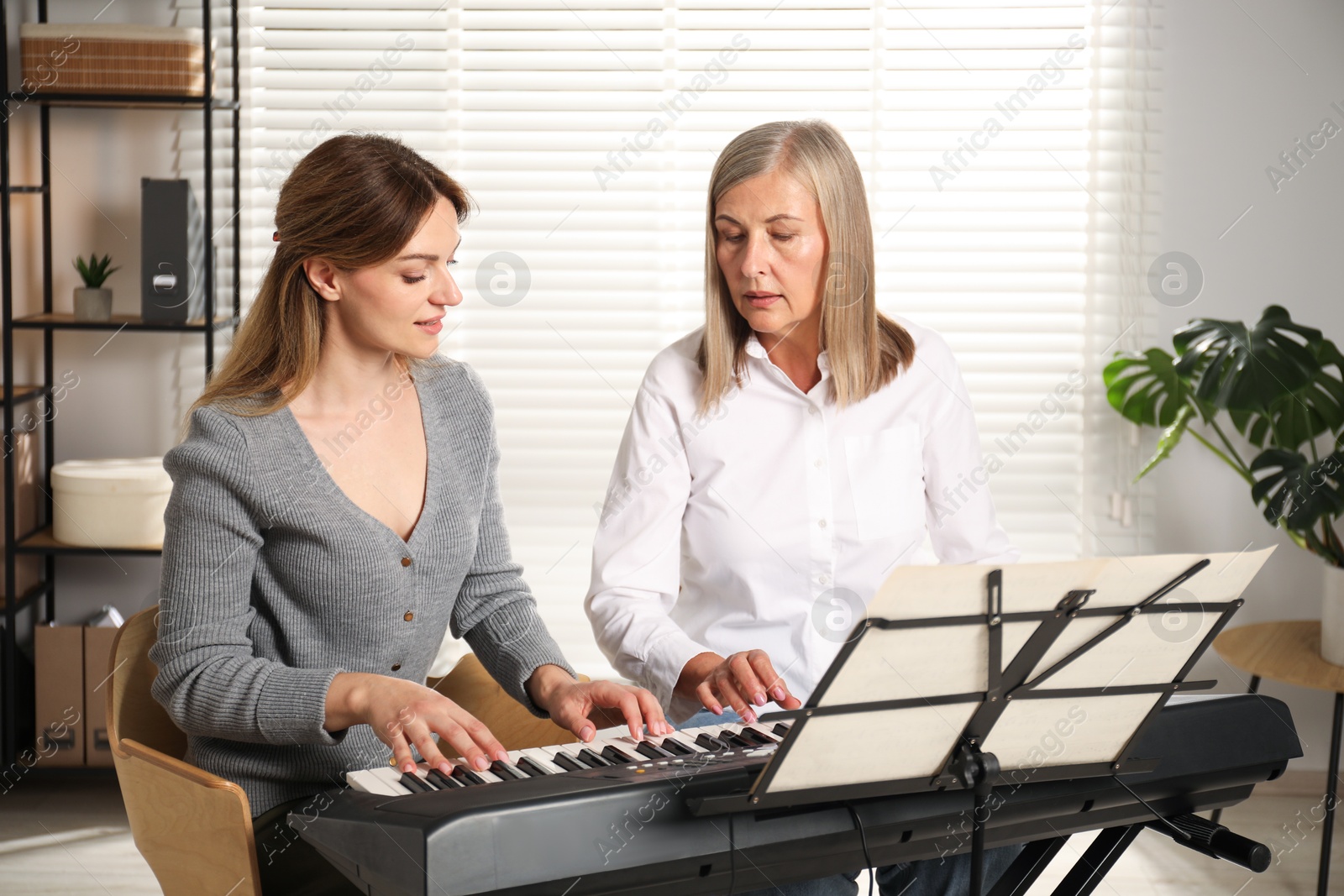 Photo of Tutor teaching woman to play piano indoors
