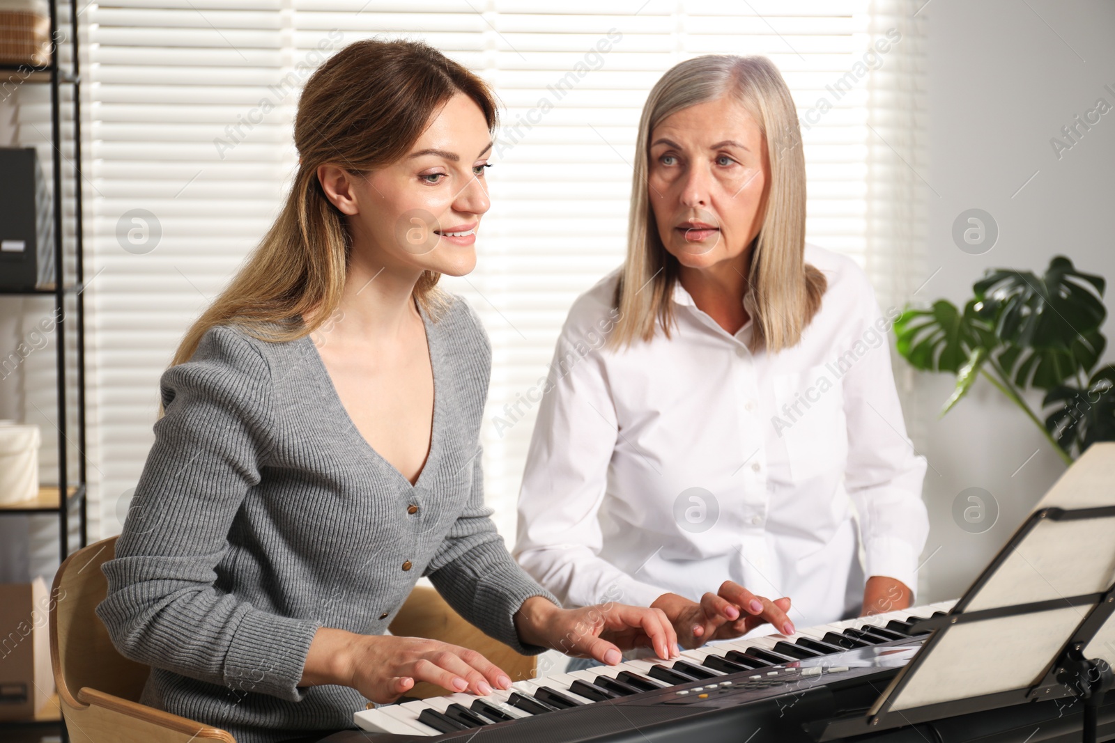 Photo of Tutor teaching woman to play piano indoors