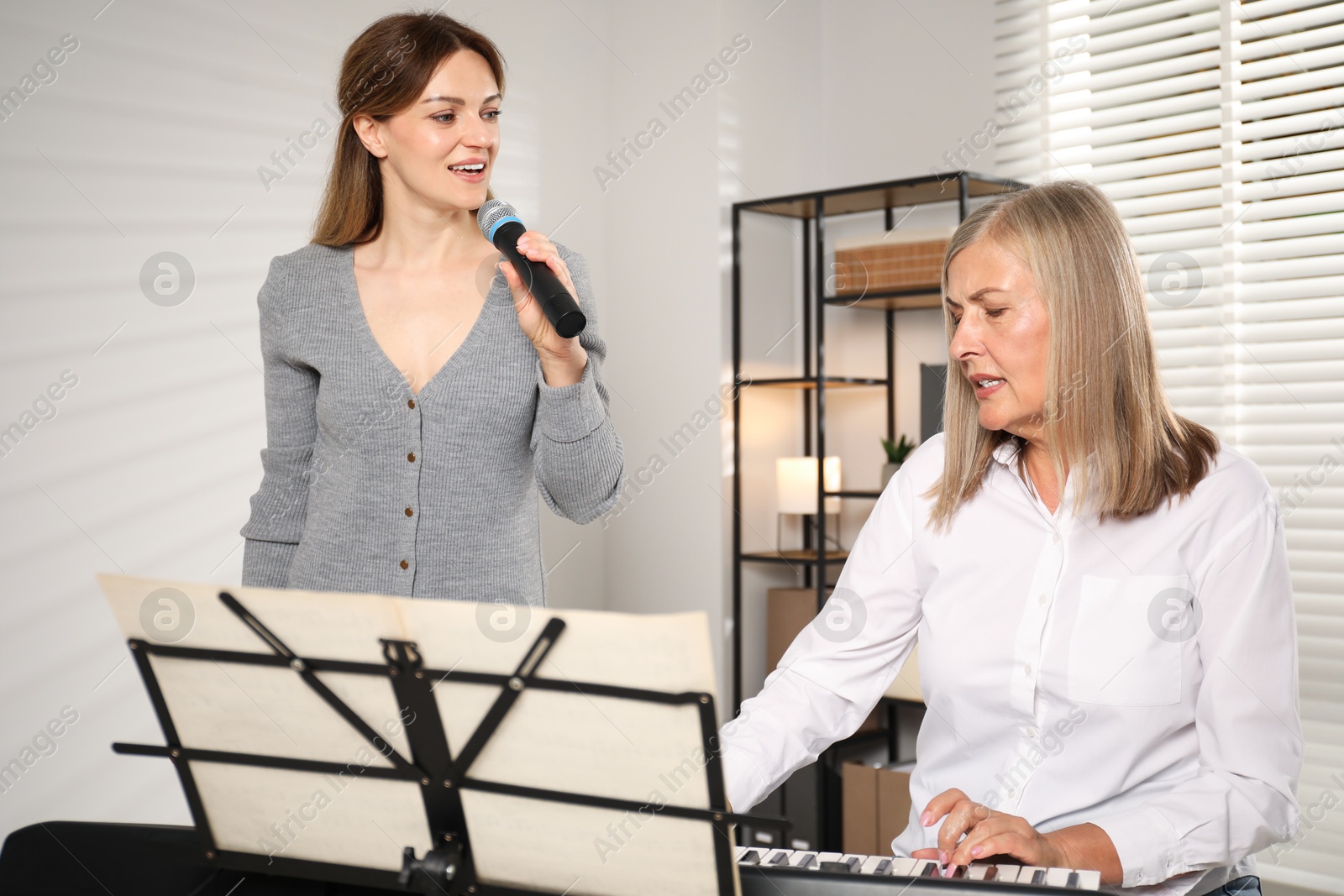 Photo of Woman learning to sing while her teacher accompanying on piano indoors