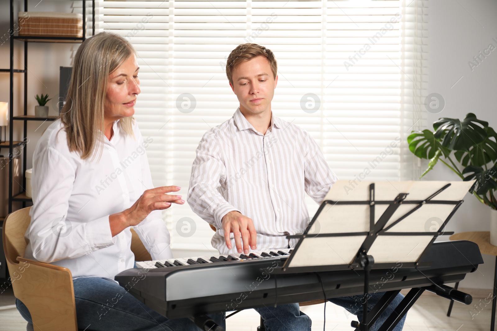 Photo of Tutor teaching man to play piano indoors