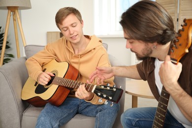 Photo of Tutor teaching man to play guitar at home