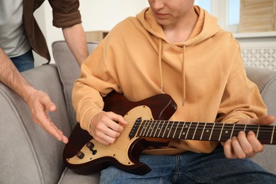 Photo of Tutor teaching man to play guitar at home, closeup