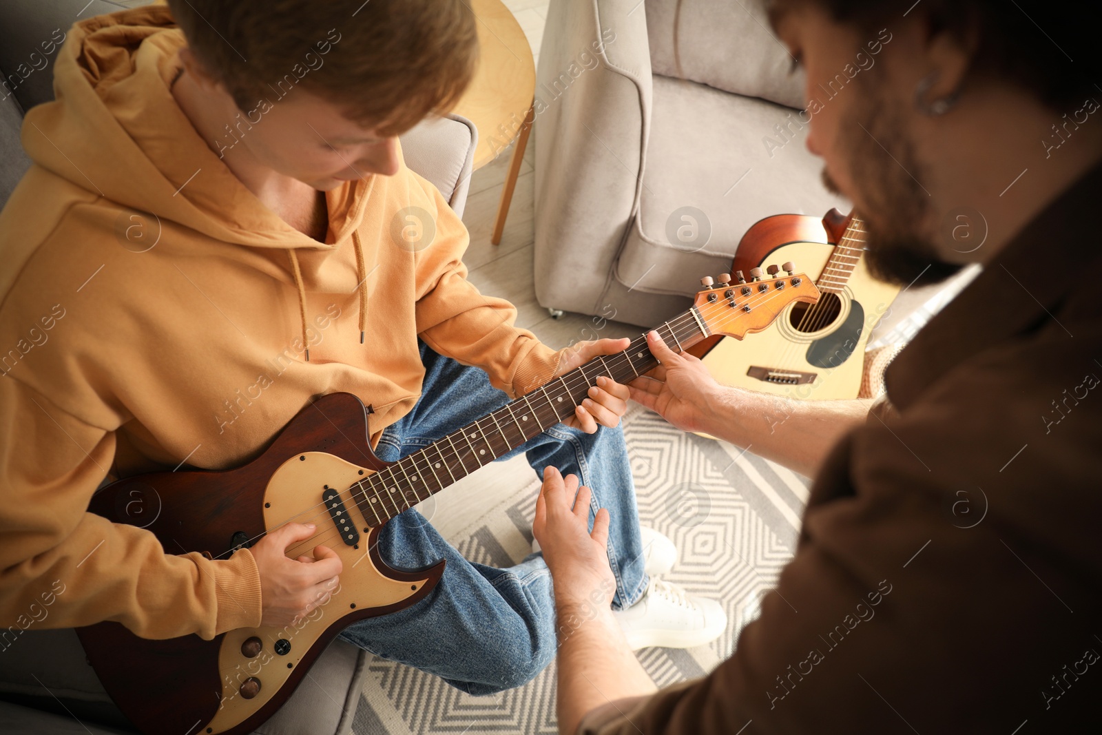 Photo of Tutor teaching man to play guitar at home, closeup
