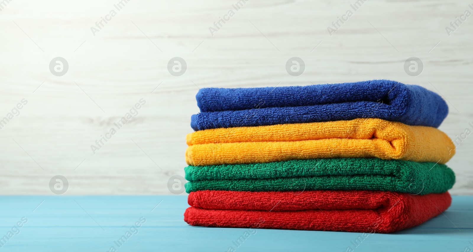Photo of Colorful fresh terry towels on blue wooden table against white background, closeup. Space for text