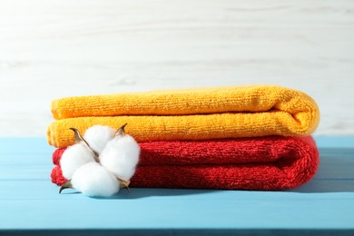 Photo of Colorful fresh terry towels and cotton flower on blue wooden table against white background, closeup