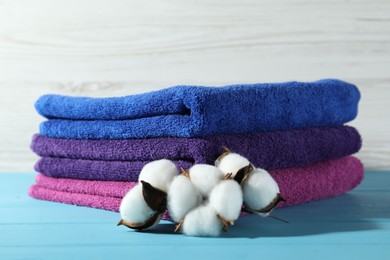Photo of Colorful fresh terry towels and cotton flowers on blue wooden table against white background, closeup