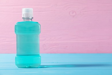 Photo of Bottle of mouthwash on blue wooden table against pink background, space for text. Oral hygiene