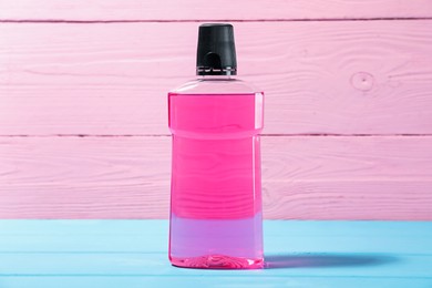 Photo of Bottle of mouthwash on blue wooden table against pink background. Oral hygiene