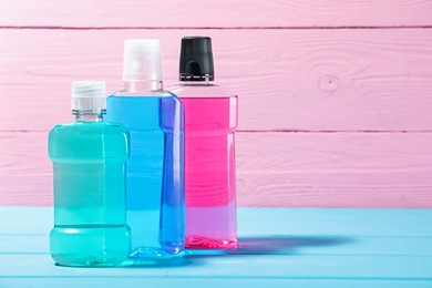 Photo of Mouthwash in bottles on blue wooden table against pink background, space for text. Oral hygiene
