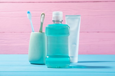 Photo of Mouthwash, toothpaste and toothbrushes on blue wooden table against pink background. Oral hygiene