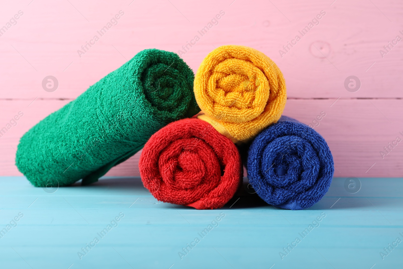 Photo of Colorful fresh terry towels on blue wooden table against pink background, closeup