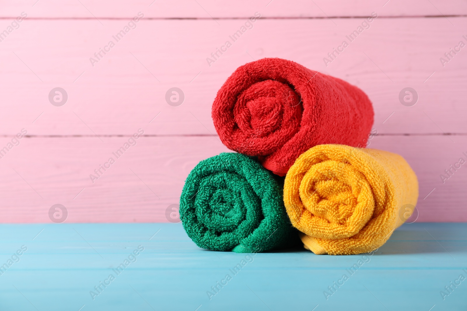 Photo of Colorful fresh terry towels on blue wooden table against pink background, closeup. Space for text