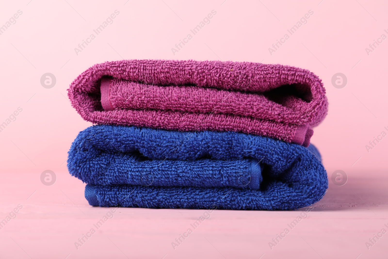 Photo of Colorful fresh terry towels on pink wooden table, closeup