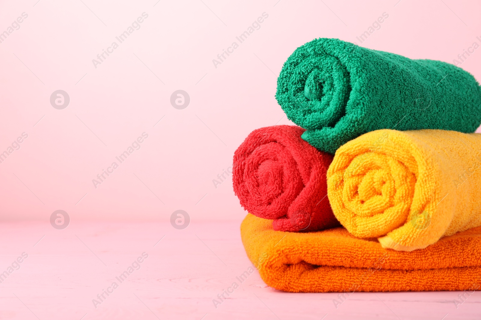 Photo of Colorful fresh terry towels on pink wooden table, closeup. Space for text