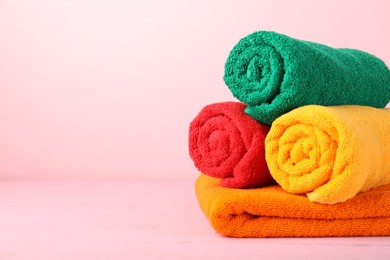 Photo of Colorful fresh terry towels on pink wooden table, closeup. Space for text
