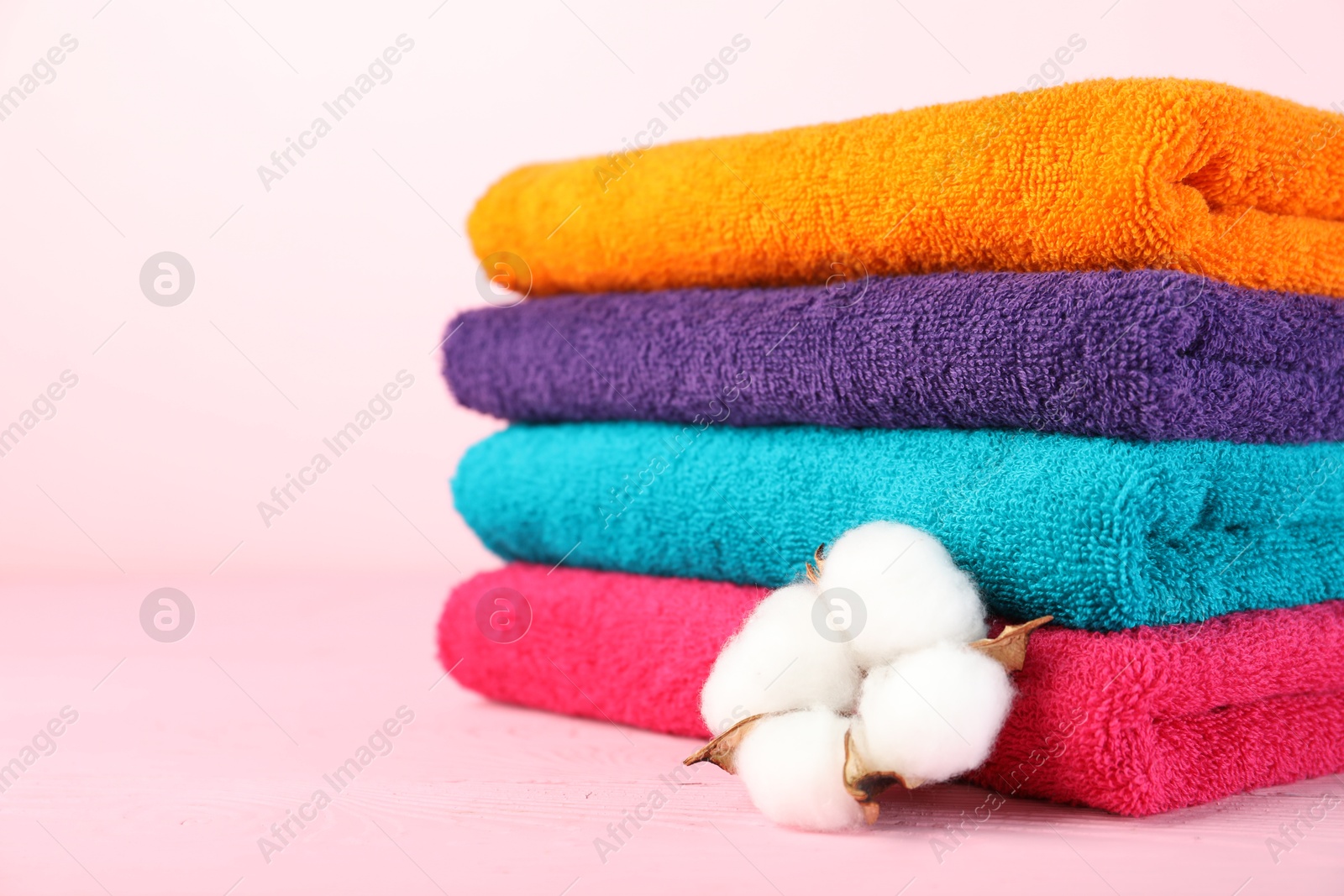 Photo of Colorful fresh terry towels and cotton flower on pink wooden table, closeup