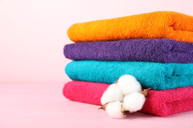 Photo of Colorful fresh terry towels and cotton flower on pink wooden table, closeup