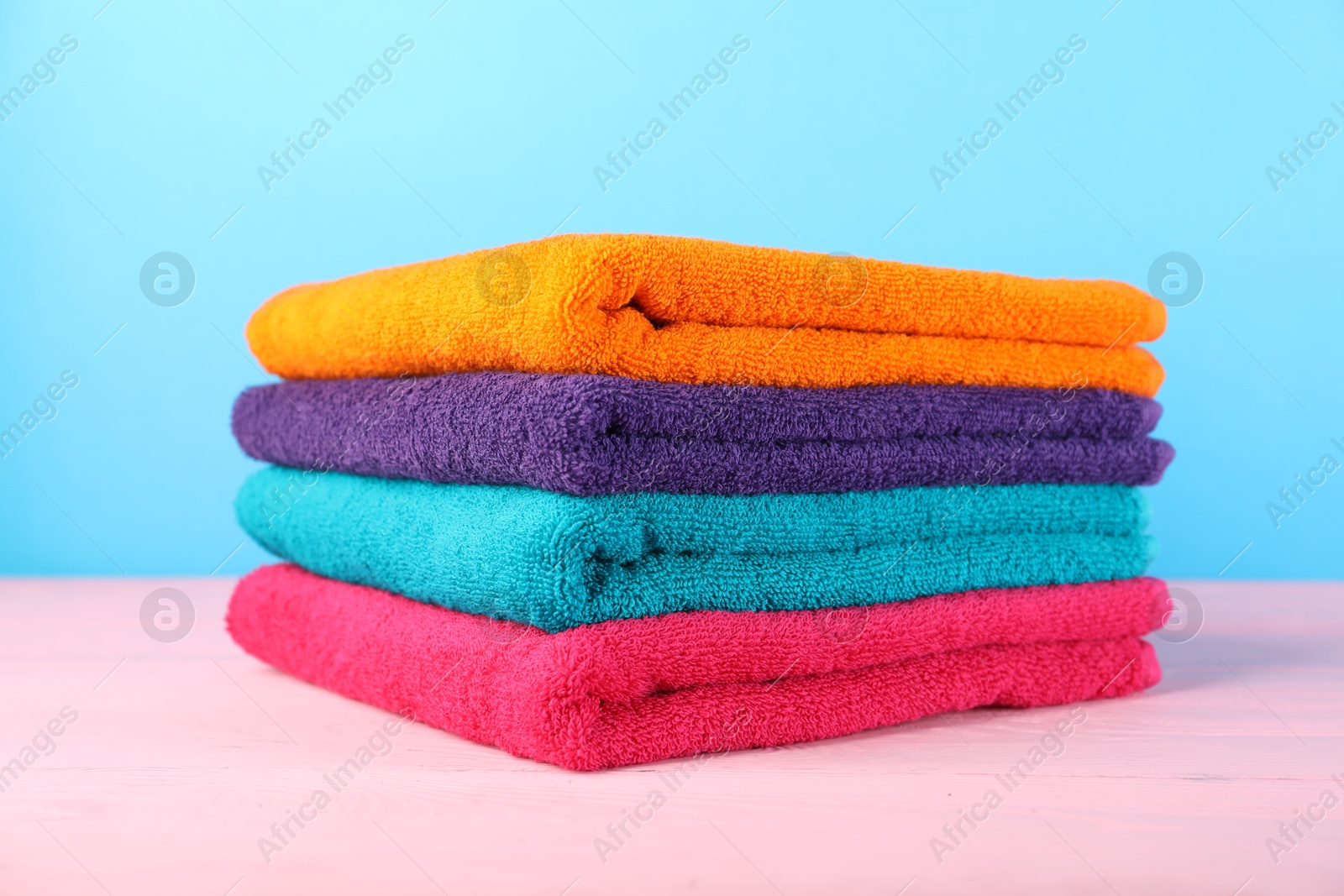 Photo of Colorful fresh terry towels on pink wooden table against blue background, closeup