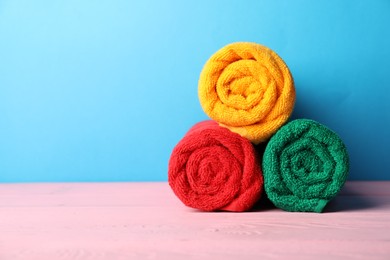 Photo of Colorful fresh terry towels on pink wooden table against blue background, closeup. Space for text