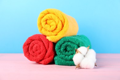 Photo of Colorful fresh terry towels and cotton flower on pink wooden table against blue background, closeup