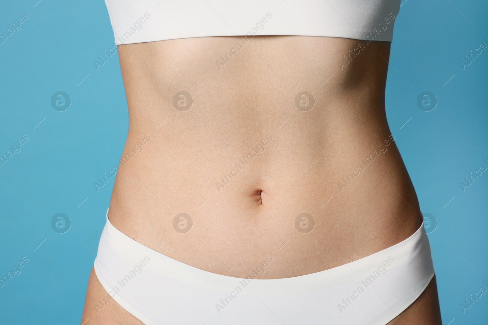 Photo of Young woman with flat belly on light blue background, closeup
