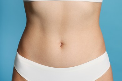 Photo of Young woman with flat belly on light blue background, closeup