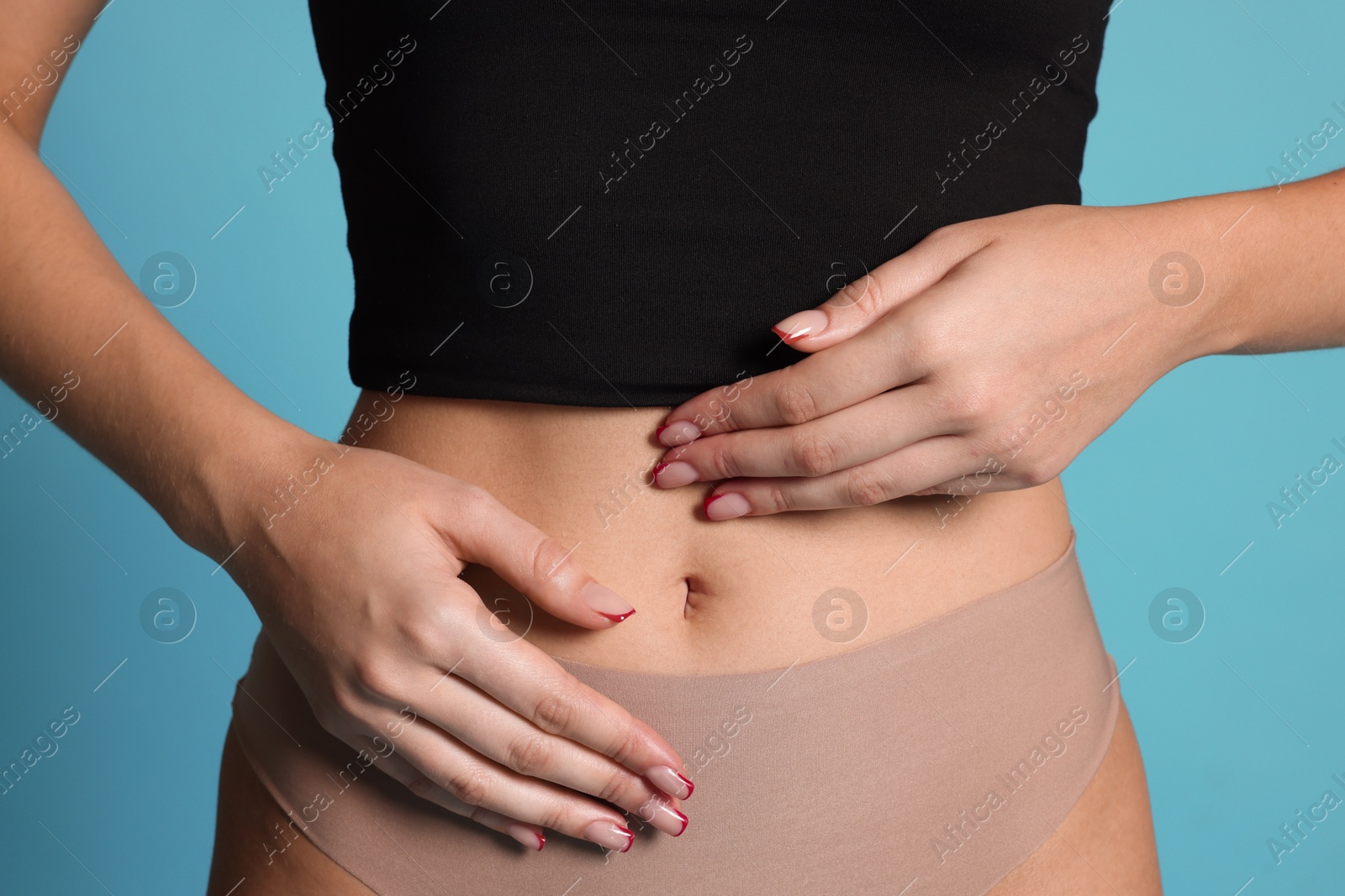 Photo of Young woman with flat belly on light blue background, closeup