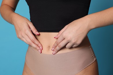 Photo of Young woman with flat belly on light blue background, closeup
