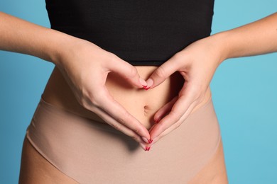 Photo of Young woman with flat belly making heart gesture on light blue background, closeup