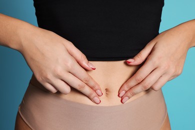 Photo of Young woman with flat belly on light blue background, closeup