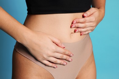 Photo of Young woman with flat belly on light blue background, closeup