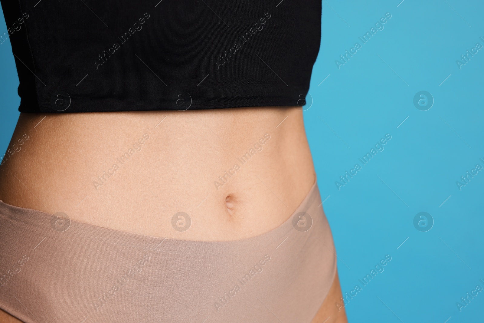 Photo of Young woman with flat belly on light blue background, closeup