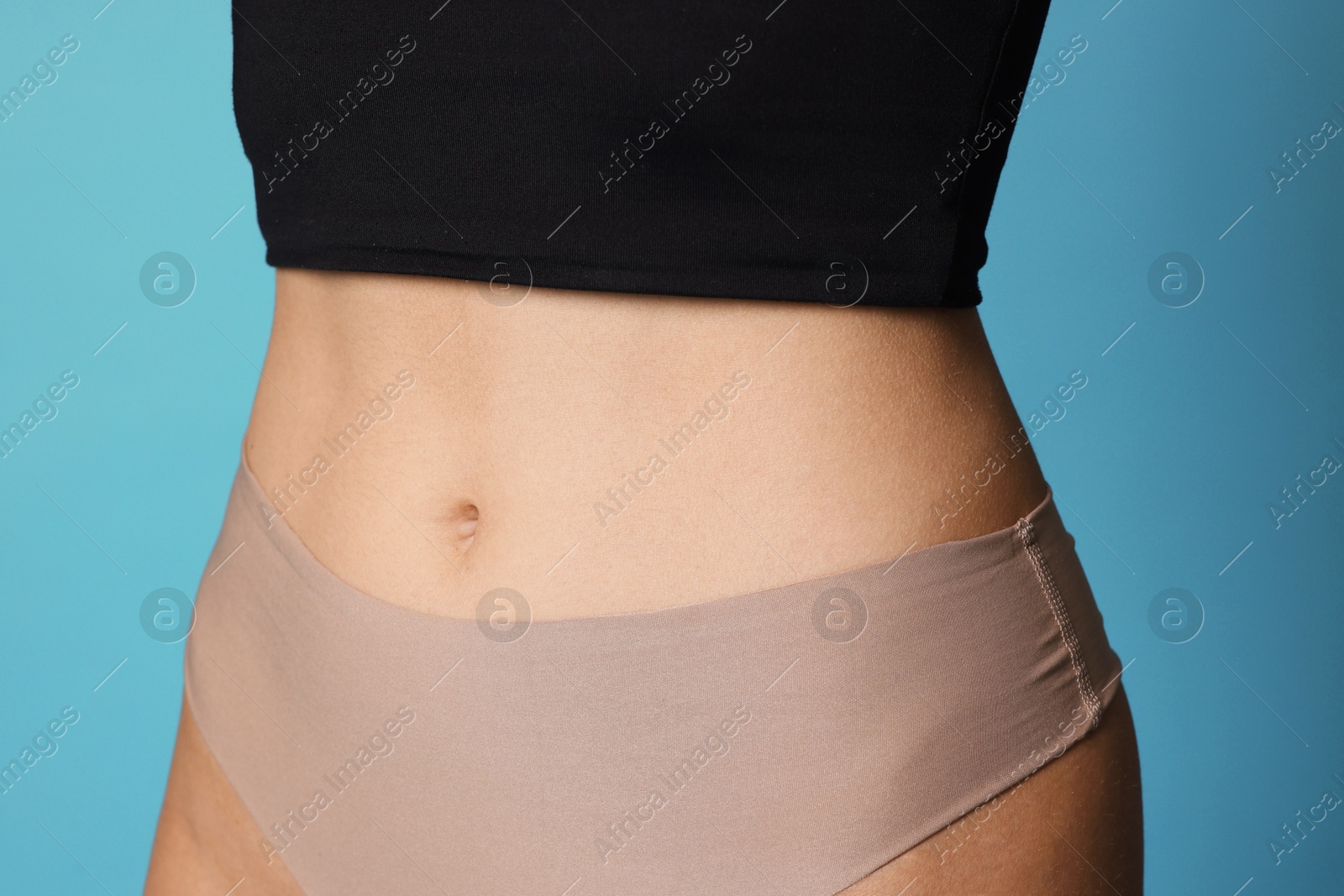 Photo of Young woman with flat belly on light blue background, closeup