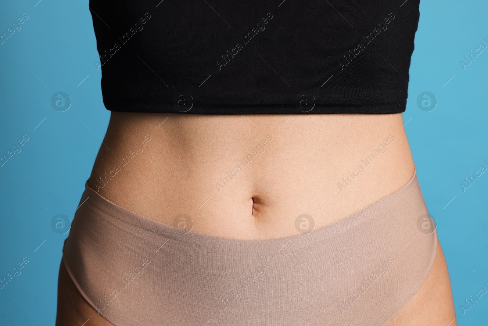 Photo of Young woman with flat belly on light blue background, closeup