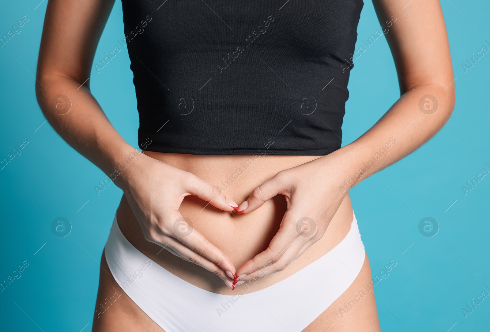 Photo of Young woman with flat belly making heart gesture on light blue background, closeup