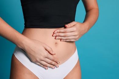 Photo of Young woman with flat belly on light blue background, closeup