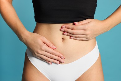 Photo of Young woman with flat belly on light blue background, closeup