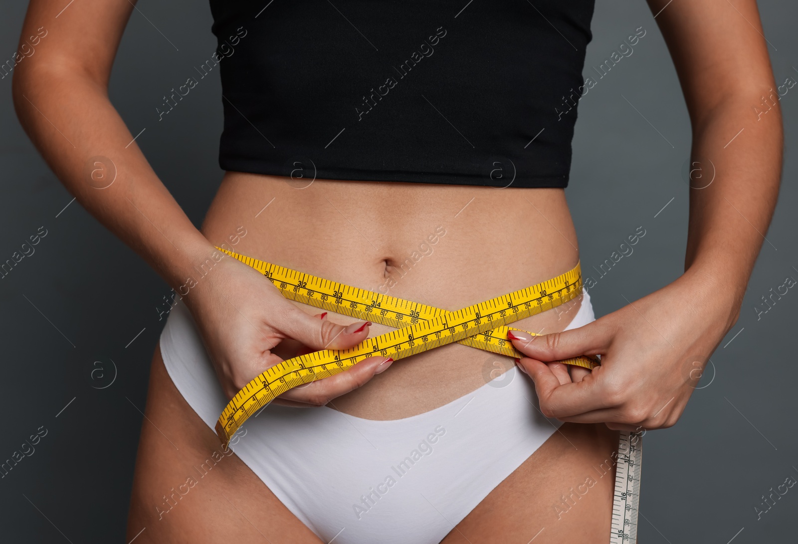 Photo of Young woman measuring her flat belly with tape on grey background, closeup