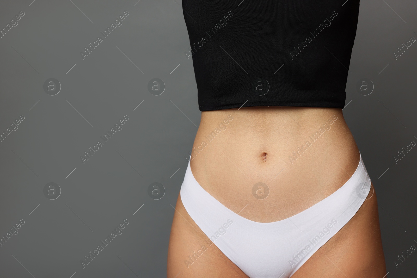 Photo of Young woman with flat belly on grey background, closeup. Space for text