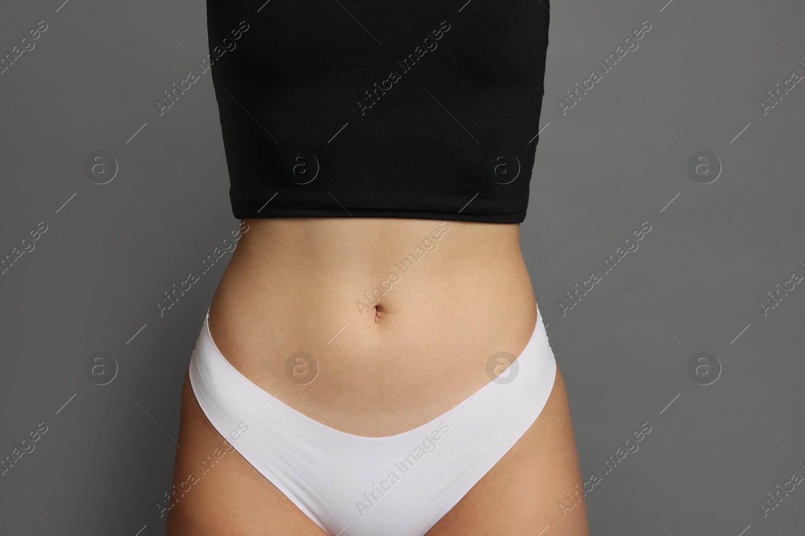 Photo of Young woman with flat belly on grey background, closeup