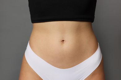 Photo of Young woman with flat belly on grey background, closeup