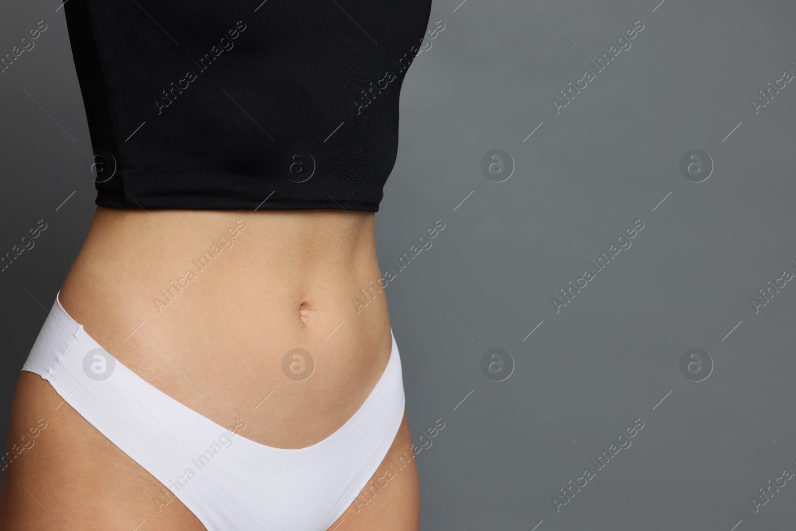 Photo of Young woman with flat belly on grey background, closeup. Space for text