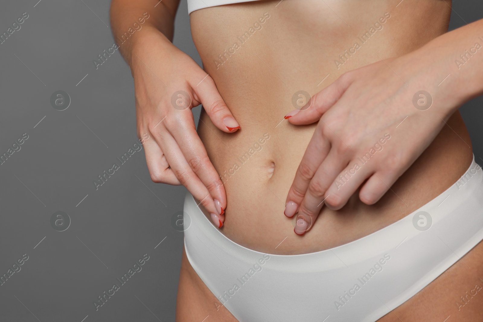 Photo of Young woman with flat belly on grey background, closeup