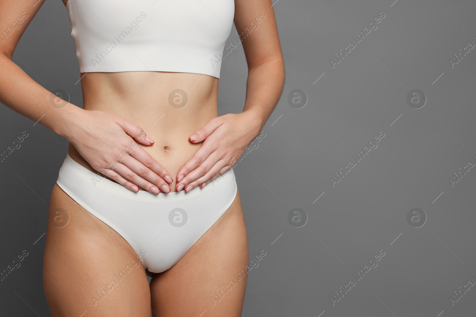 Photo of Young woman with flat belly on grey background, closeup. Space for text