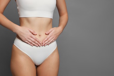 Photo of Young woman with flat belly on grey background, closeup. Space for text